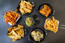 French Fries, Sweet Potato Fries, Guacamole, Chicken Wings And Tortilla Chips On A Black Table