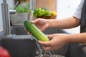 Young woman washing cucumber to remove pesticides before cooking in kitchen. Fruit and vegetables washing concept.