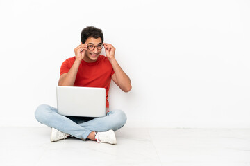 Wall Mural - Caucasian handsome man with a laptop sitting on the floor with glasses and surprised