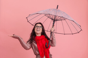 Wall Mural - Portrait of smiling beautiful woman in glasses holding umbrella on pink background