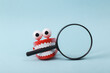 Funny toy clockwork jumping teeth with eyes holding magnifying glass on blue background.
