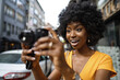 © fotofabrika - Smiling African american woman using professional camera at a street