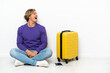 © luismolinero - Young blonde man with suitcase sitting on the floor laughing in lateral position