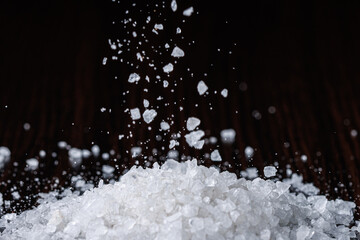 Coarse-grained sea salt is poured into a pile against the background of a black table. Selective focus. Close-up.