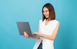© sitthiphong - Studio shot of cheerful beautiful Asian woman holding laptop with typing on keyboard on blue background.