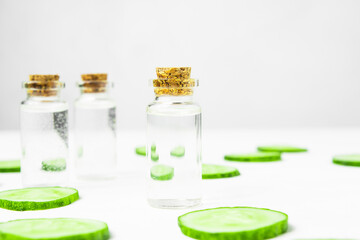  Serum, lotion for skin care and moisturizing with fresh cucumber slices on a white wooden background.