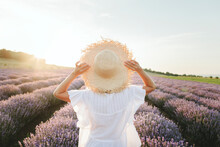 Woman Wearing Hat Standing In Lavender Field At Sunset