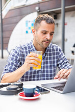 Mature Freelancer With Orange Juice Using Laptop At Cafe