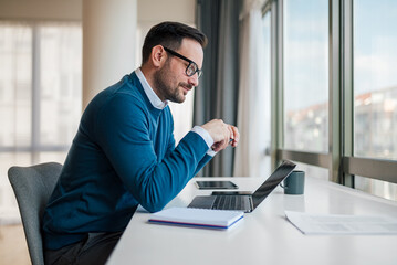 Wall Mural - smiling entrepreneur analyzing successful plan on laptop while working at office