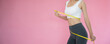 Slim woman in sportswear measures her waist using tape measure on pink background. diet woman and achieve weight loss goals