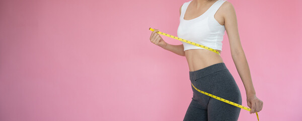 slim woman in sportswear measures her waist using tape measure on pink background. diet woman and ac