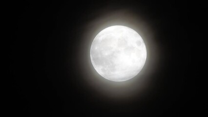 Wall Mural - Glowing huge full moon as seen from earth through the clouds against starry night sky. Large full moon moves across the sky, moon makes its way from bottom left frame to top right.