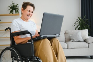 Poster - Middle age woman using laptop sitting on wheelchair at home