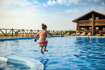 Wall Mural - A girl with swimming goggles jumps into a pool with clear water on the background of a warm summer sunny sunset