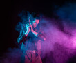 © Ulia Koltyrina - A guy in a cyberpunk image, holding a gun in his hands. Futuristic character in smoke. A young man in neon lighting on a black background