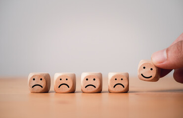 Poster - Hand holding smile face which print screen on wooden cube block among sad face for positive thinking mindset concept.