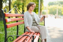 An Elderly Woman Sitting On Bench In Summer Park