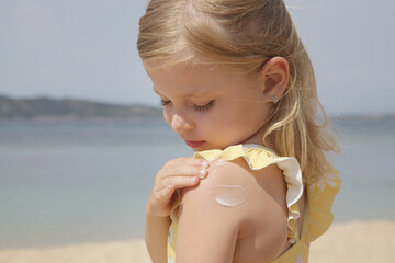 cute little toddler girl applying sunscreen protection cream on the beach. sun blocking lotion for p