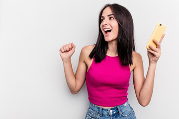 Young caucasian woman holding mobile phone isolated on white background raising fist after a victory, winner concept.