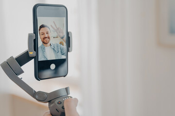 Male hand holding gimbal stabilizer with smartphone and smiling at camera