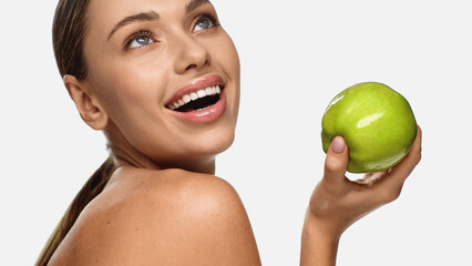 Poster - portrait of happy young woman looking away while holding green apple isolated on white.