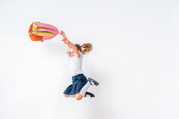 happy schoolgirl in uniform with a backpack jumps on a white background in the studio. the little girl is ready for school. conceptual school. the holidays begin. Advertising discounts