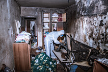 A Specialist In A Protective Suit From A Cleaning Company Cleans A Destroyed Housing After A Fire