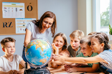 Canvas Print - A group of pupils children with teacher sitting on the desk in class, learning. School teacher and children using globe.