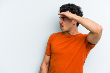 Wall Mural - Young caucasian man isolated on blue background looking far away keeping hand on forehead.