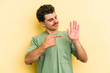 Wall Mural - Young caucasian man isolated on yellow background smiling cheerful showing number five with fingers.