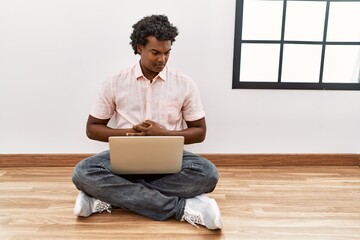 Poster - African man with curly hair using laptop sitting on the floor with hand on stomach because nausea, painful disease feeling unwell. ache concept.