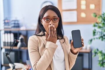 Sticker - African young woman holding smartphone showing blank screen covering mouth with hand, shocked and afraid for mistake. surprised expression