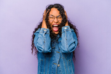 Young hispanic woman isolated on purple background covering ears with hands trying not to hear too loud sound.