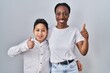 © Krakenimages.com - Young mother and son standing together over white background doing happy thumbs up gesture with hand. approving expression looking at the camera showing success.
