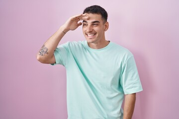 Poster - Handsome hispanic man standing over pink background very happy and smiling looking far away with hand over head. searching concept.