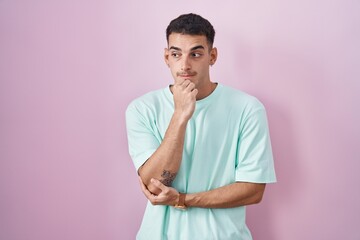 Wall Mural - Handsome hispanic man standing over pink background looking stressed and nervous with hands on mouth biting nails. anxiety problem.