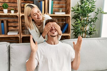 Poster - Woman surprising her boyfriend with hands on eyes at home.