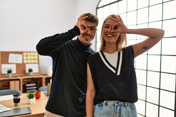 Two beautiful business workers wearing business style standing at the office smiling happy doing ok sign with hand on eye looking through fingers