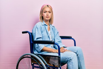 Wall Mural - Beautiful blonde woman sitting on wheelchair relaxed with serious expression on face. simple and natural looking at the camera.