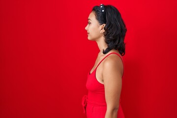 Sticker - Young hispanic woman standing over red background looking to side, relax profile pose with natural face with confident smile.