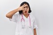 © Krakenimages.com - Young hispanic doctor woman wearing stethoscope over isolated background peeking in shock covering face and eyes with hand, looking through fingers with embarrassed expression.
