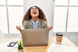 © Krakenimages.com - Beautiful hispanic business woman sitting on desk at office working with laptop crazy and mad shouting and yelling with aggressive expression and arms raised. frustration concept.