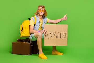 Sticker - Full size photo of positive hippy person sitting suitcase thumb up hitchhike isolated on green color background