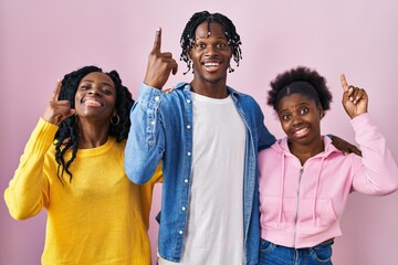 Canvas Print - Group of three young black people standing together over pink background smiling amazed and surprised and pointing up with fingers and raised arms.