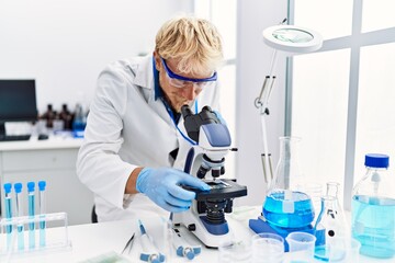 Poster - Young caucasian man wearing scientist uniform using microscope at laboratory