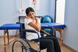 Fototapeta Przestrzenne - Young hispanic woman sitting on wheelchair at physiotherapy clinic hugging oneself happy and positive, smiling confident. self love and self care