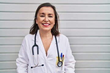 Wall Mural - Middle age hispanic woman wearing doctor uniform and stethoscope looking positive and happy standing and smiling with a confident smile showing teeth