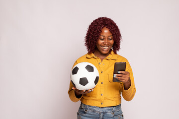 pretty black lady holding a soccer ball using her phone