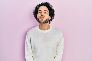 Wall Mural - Handsome hispanic man wearing casual white sweater looking at the camera blowing a kiss on air being lovely and sexy. love expression.