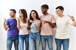 © Krakenimages.com - Group of young people standing together over isolated background smiling with happy face looking and pointing to the side with thumb up.
